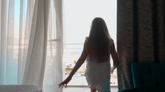 Tourist girl entering on balcony with sea view in room. Traveling girl enjoying beautiful landscape on room balcony. Gitl standing on resort appartment balcony