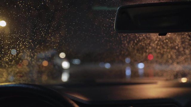 Beautiful background of front car window in raindrops cleaning by windscreen wiper at late night