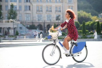 Fototapeta na wymiar Curly red-haired woman riding bike after going to supermarket