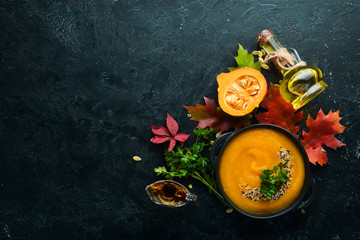 Pumpkin soup with pumpkin and colored autumn leaves. flat lay. On a black stone background. Top view. Free space for your text.