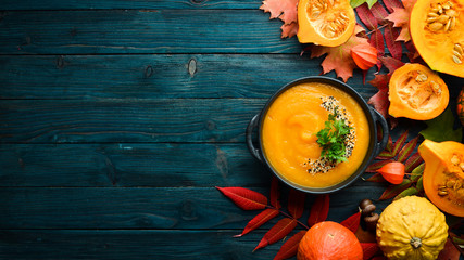 Pumpkin soup with pumpkin and colored autumn leaves. flat lay. On a blue wooden background. Top...