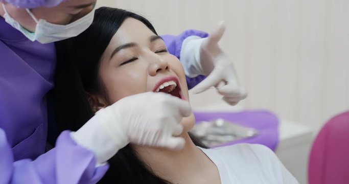 Woman in a patient in a dental clinic. Dentist in an uniform and latex gloves is flossing her teeth with a help of a dental floss.