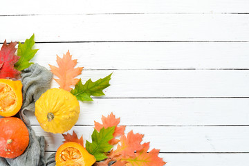 Fresh colored pumpkins and colored autumn leaves. Autumn vegetables. flat lay. On a white wooden background. Top view. Free space for your text.