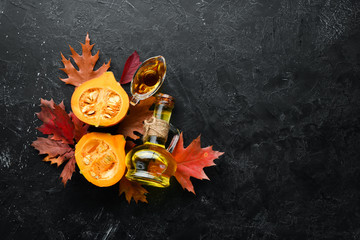 Pumpkin oil and pumpkins. Autumn vegetables. flat lay. On a black stone background. Top view. Free space for your text.
