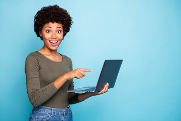Fototapeta na wymiar Photo of cute stylish trendy black model pointing at laptop recommending you to purchase it requesting to follow on social media wearing hreen sweater jeans denim isolated vivid color blue background