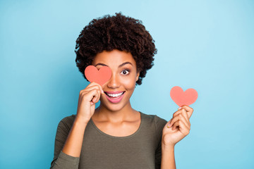 Close up photo of amazed excited emotions expression afro american girl hold little paper card close cover her face have fun on date for 14-february wear green sweater isolated over blue color