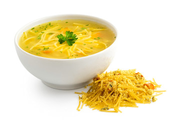 Instant chicken noodle soup in a white ceramic bowl next to a pile of dry instant soup isolated on white. Parsley garnish.