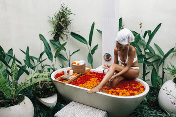 Woman relaxing in outdoor bath with flowers in Bali spa hotel.