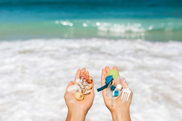 Concept of choice: save nature or continue to use disposable plastic. One hand holding beautiful shells, in the other - plastic waste. Ocean and tropical beach on background. Environmental pollution - 294571529