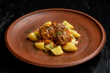 Meatballs with potato wedges on a beautiful clay plate.