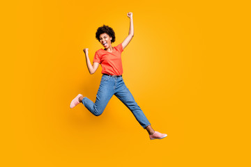 Fototapeta na wymiar Full size photo of crazy funky delighted lady jump celebrate victory in lottery raise her fists scream yeah wear red t-shirt denim jeans sneakers isolated over yellow color background