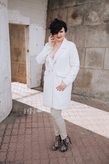 Young beautiful stylish woman in white wool coat walking down the street. Plus size short hair adult girl posing alone.