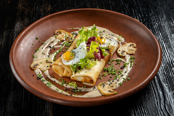 Rolled pancakes on top lies scrambled eggs. Beautiful clay plate.