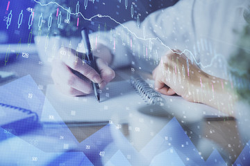 Financial forex graph displayed on hands taking notes background. Concept of research. Double exposure