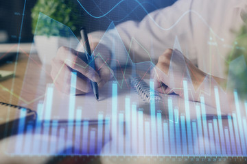 Financial forex graph displayed on hands taking notes background. Concept of research. Multi...