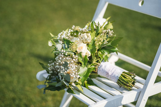 Wedding bouquet made of white roses and greenery on a chair. Outdoor weddng ceremony