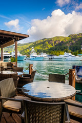 Dining table and chairs at small restaurant decking by marina of Eden Island, Mahe, Seychelles, vertical composition