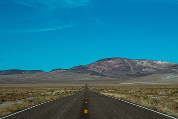 Long and Lonely road in the desert of Nevada leading towards a mountain range with nobody around