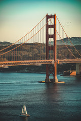 Fototapeta na wymiar Golden Gate bridge San Francisco, California in the sunset with a sailing boat underneath it