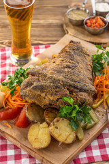 Pork knuckle roast served with potato and pickled vegetables and glass of beer on wooden table