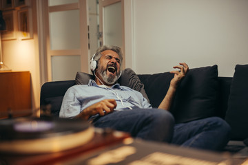 mid aged man relaxing home and listening music on record player - obrazy, fototapety, plakaty