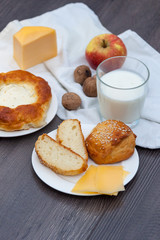 Fresh homemade buns with sesame and cheese on wooden background with glass of milk, apple, nuts.