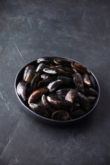 Bowl with fresh raw mussels on dark background