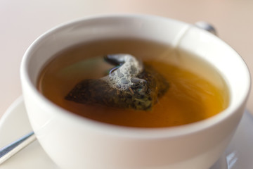 White mug cup of herbal green tea with a teabag inside close up