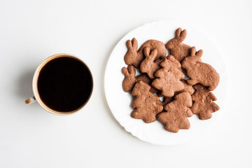 A cup of coffee and Christmas chocolate cookies on a white plate on a white background, top view