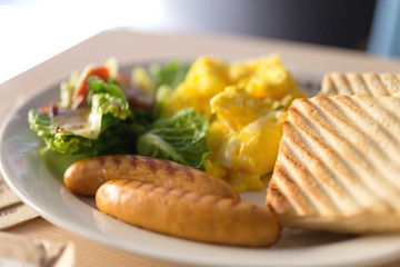Close up breakfast with sausages, bread, scrambled eggs and vegetables salad on white plate, macro