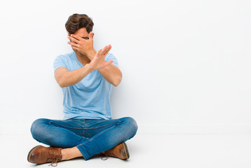 young handsome man covering face with hand and putting other hand up front to stop camera, refusing...