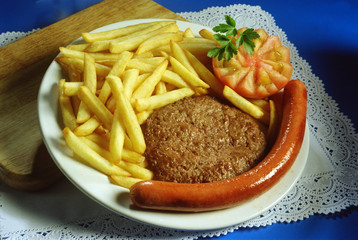 Plato con una hamburguesa, una salchicha frankfurt, patatas fritas y tomate.