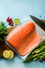 fresh salmon slice on a wooden cutting board with fresh aromatic herbs and asparagus on the table. cooking recipe. food background. fresh fish products
