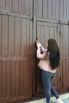 Young cute pregnant girl in pink warm down jacket trying to open the key lock. Late autumn, the cold is coming. toned photo. Very big door