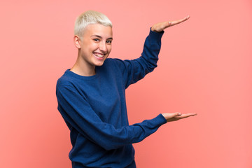 Teenager girl with white short hair over pink wall holding copyspace to insert an ad