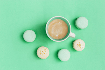 Delicious macaroons with almond and hot coffee cappuccino in big mug on bright mint paper surface. Sweet food background. Top view.