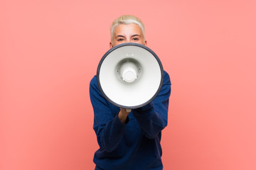 Teenager girl with white short hair over pink wall shouting through a megaphone