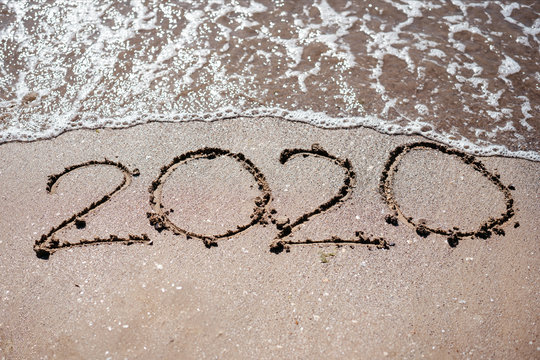2020 written in beach sand and washed by a wave