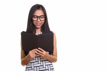 Young happy Asian teenage nerd girl smiling while reading book
