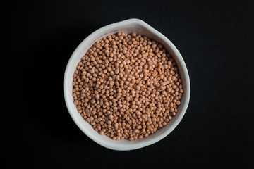 Mustard seeds spice in white ceramic bowl isolated on black background