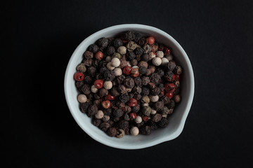 Peppercorn pepper spice in a white ceramic bowl isolated on black background