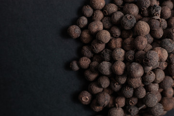 Spice allspice black peppercorns scattered on a black background