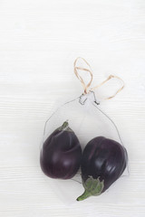 Ripe fresh eggplants in eco natural bags sewing from mesh cloth on light background with copy space. Zero waste food shopping concept. View from above.