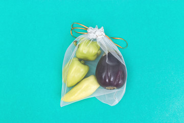Green bell peppers and eggplants in eco natural bags sewing from mesh cloth on mint paper...