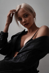 Fototapeta premium Attractive cute young model with blonde hair and red lips sexy posing on white background in studio. Sexy hot woman in lingerie, leather jacket. Portrait of beauty stylish girl