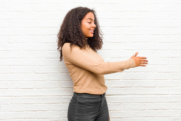 young black woman smiling, greeting you and offering a hand shake to close a successful deal, cooperation concept against brick wall © kues1