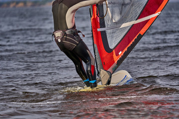 Naklejka premium A male athlete is interested in windsurfing. He moves on a Sailboard on a large lake on an autumn day.