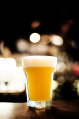 The large glass of yellow draft beer with bokeh of bar in the background for copy space.