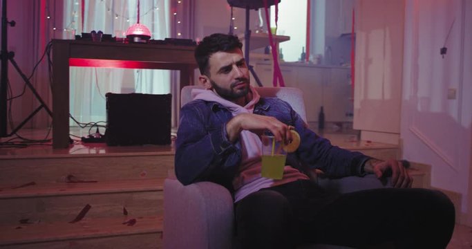 Seriously man at home party enjoying the time chilling and feeling relaxed drinking some cocktail , lots of decorations stuff around