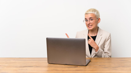 Teenager girl with short hair with a laptop frightened and pointing to the side